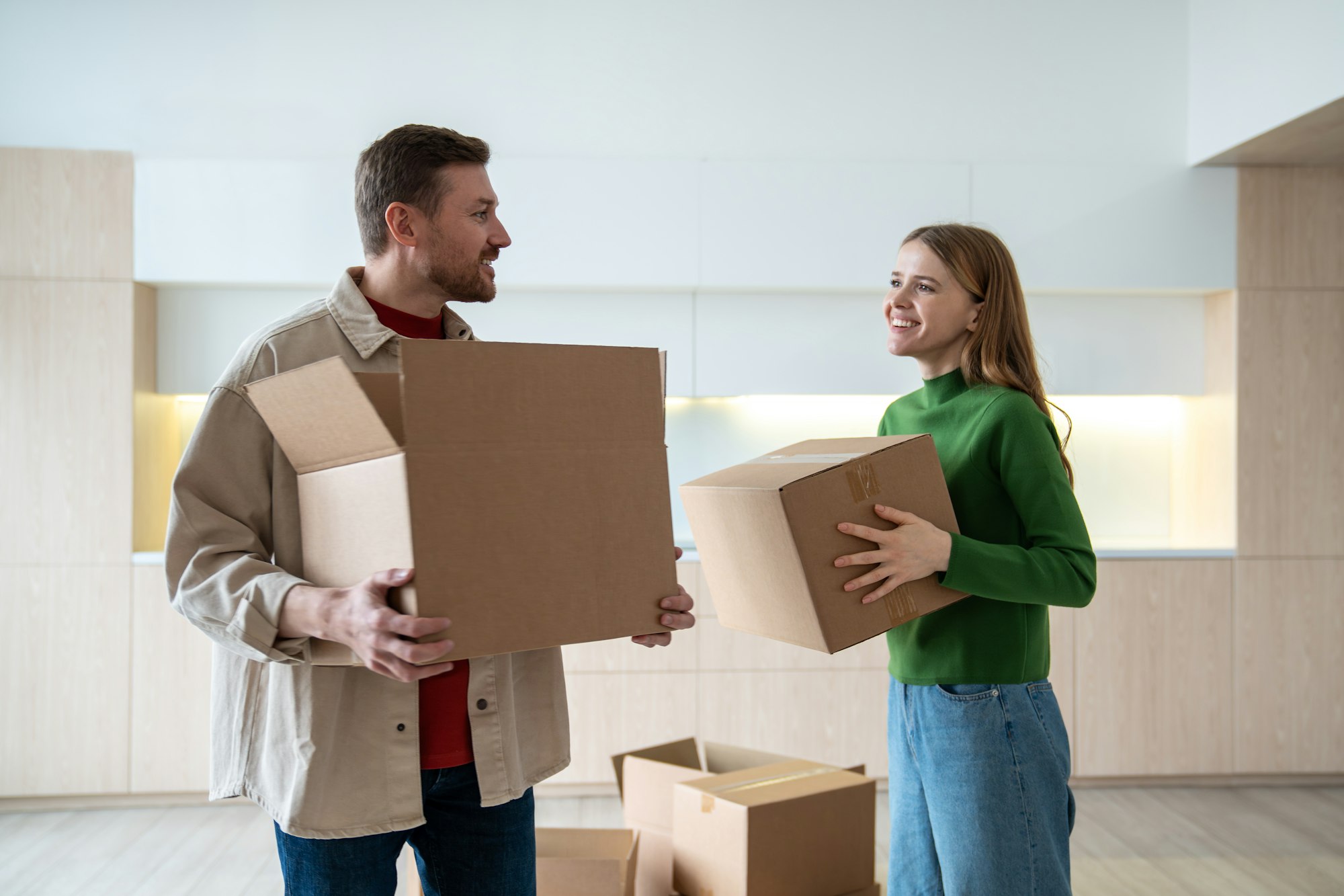 Happy new homeowners tenants renters young couple pleased man and joy woman carrying boxes to room