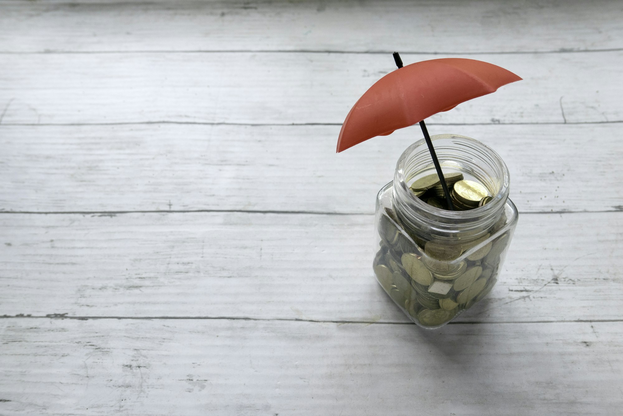 Financial security and investment concept. Red umbrella over a jar of coins.