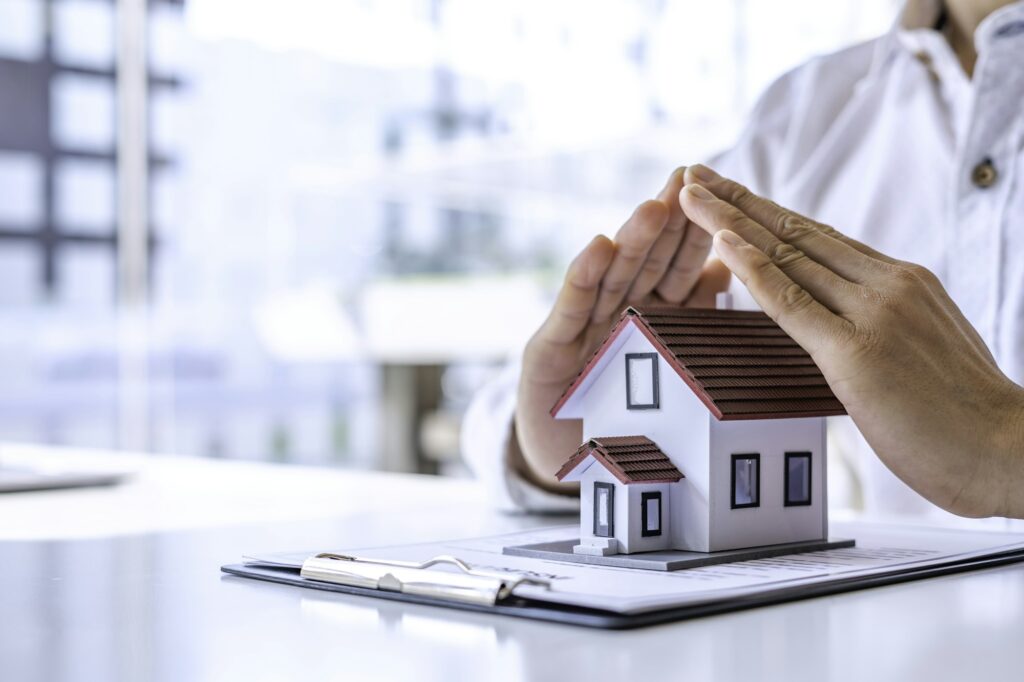 Home security and insurance concept - A close-up view of a man defending a home model by hand on a t