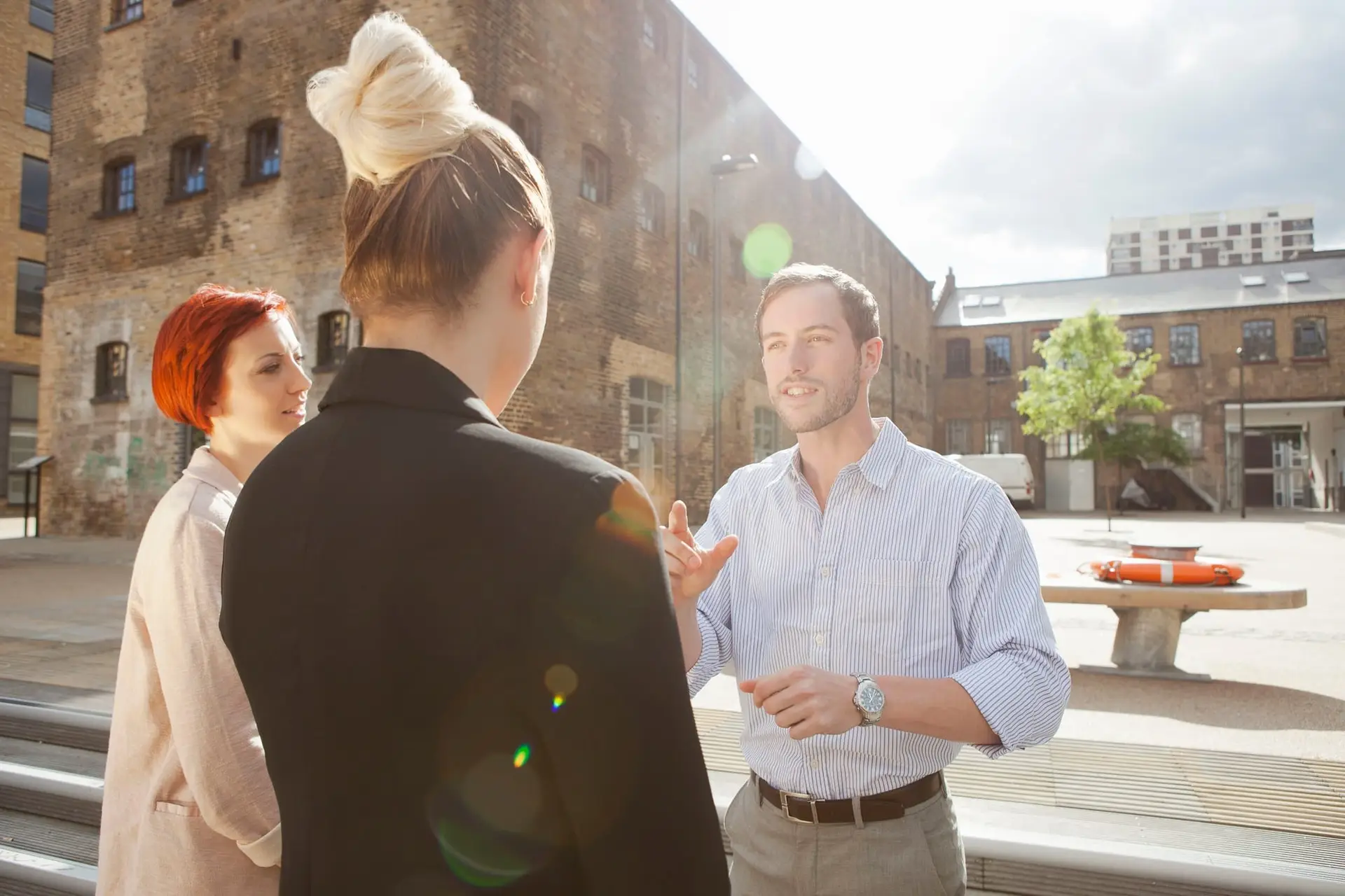 Three young people talking, building in background, East London, UK