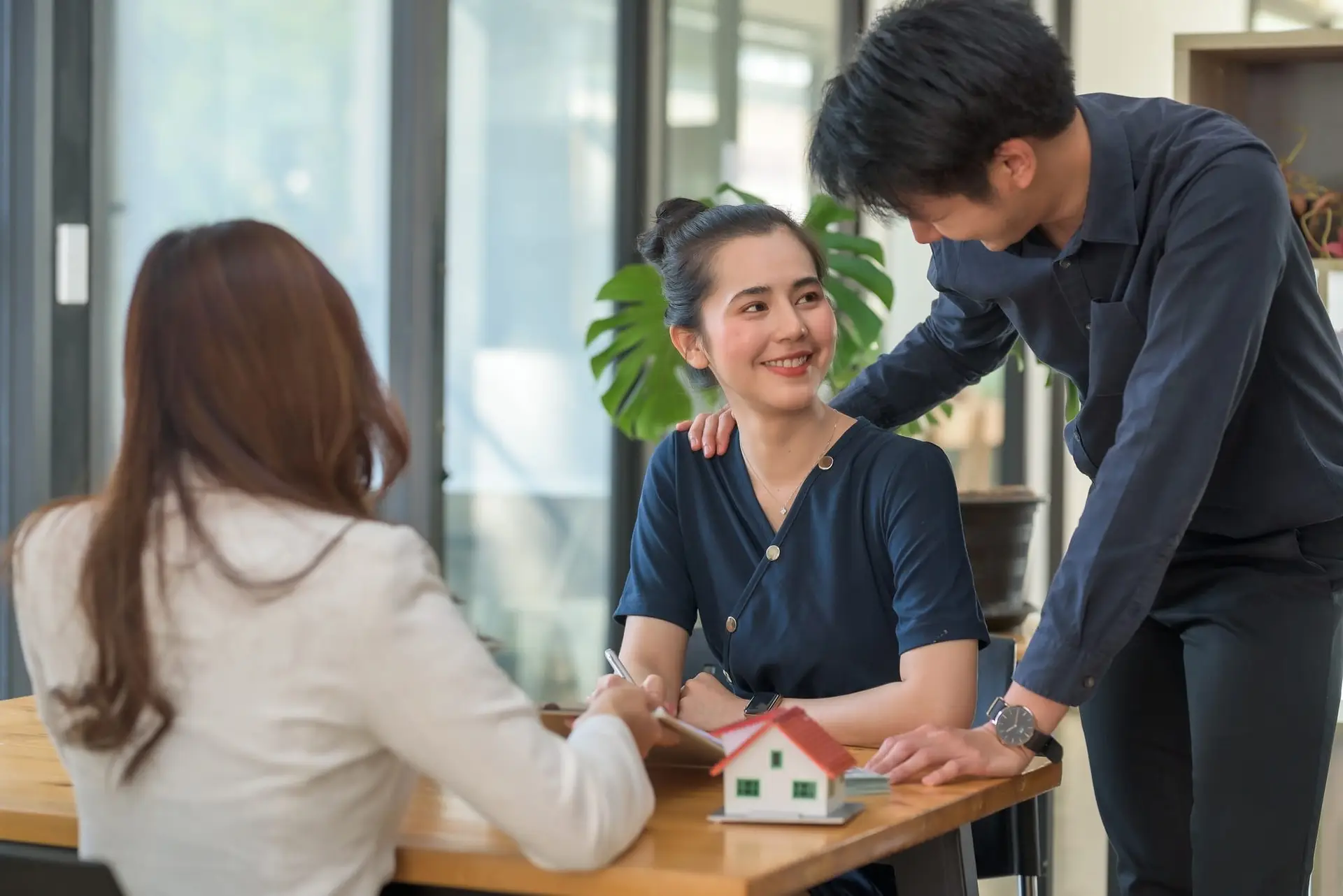 Real estate agent discussing contract with a couple, property model on desk