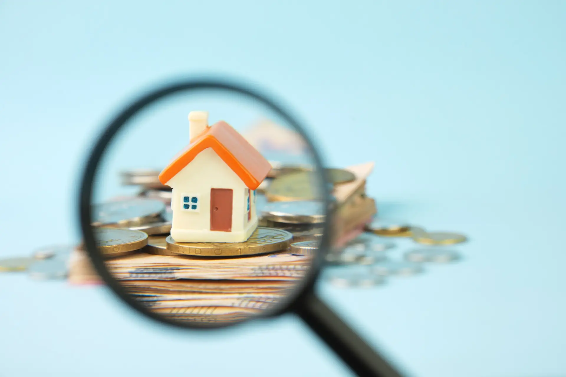 Miniature house and money under a magnifying glass.