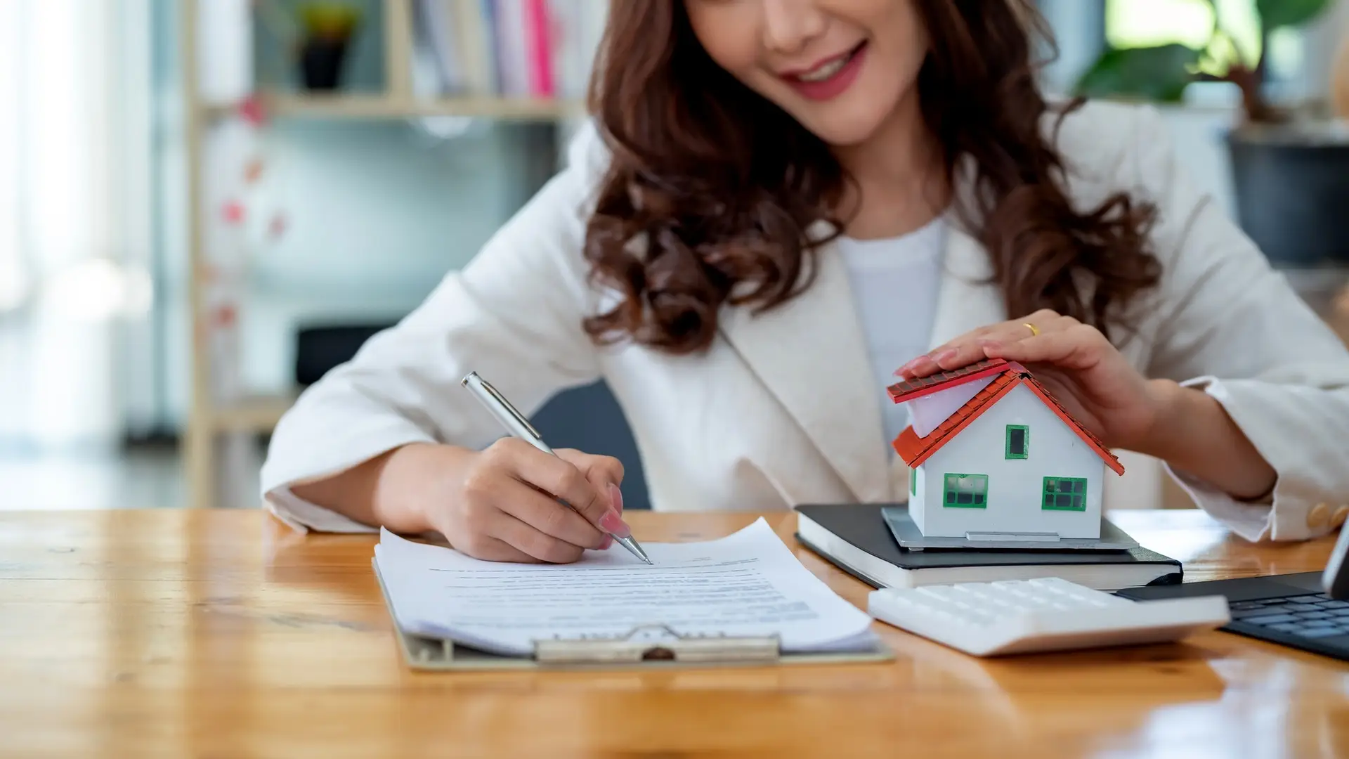 Businesswoman signing contract while holding house model