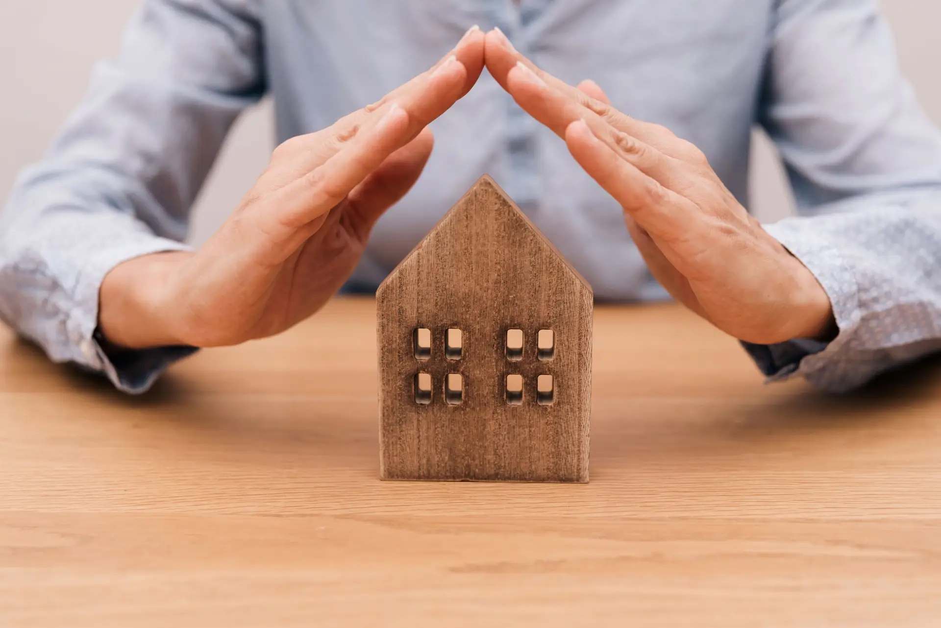 close up of Hands forming roof over wooden house model on wooden desk, home insurance concept